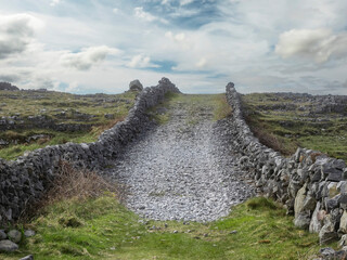 Small rough stone road up hill and fences and view on stunning landscape of Aran island, county...