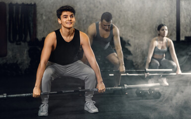 Smiling handsome sporty guy performing deadlift with barbell during intense group workout in gym