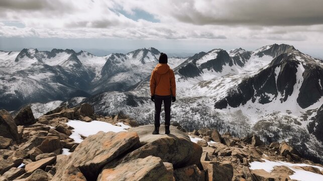 A person standing on a mountain peak with a view of a snowy mountain range. Generative AI