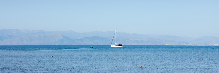 Fototapeta premium Fantastic seaside view at the sea with the alone yacht on the horizon, Corfu island, Greece. Sunny day, minimalism, calm and silence.