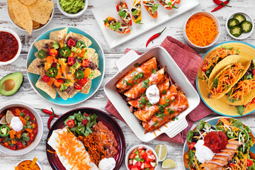 Mexican food table scene. Overhead view on a white wood background. Tacos, burrito plate, nachos,...