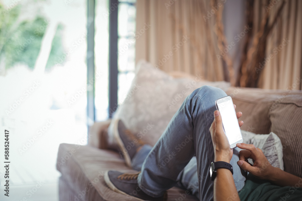 Poster Low section of man using mobile phone while relaxing on sofa