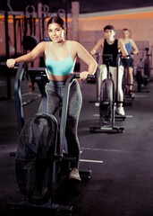 Fototapeta na wymiar Focused motivated young girl leading healthy active lifestyle doing cardio workout on exercise bike in gym