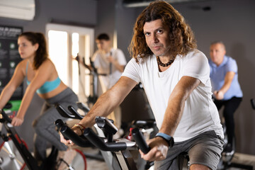 Fototapeta na wymiar Focused sporty adult man working out on stationary bicycle in gym. Physical activity and fitness concept
