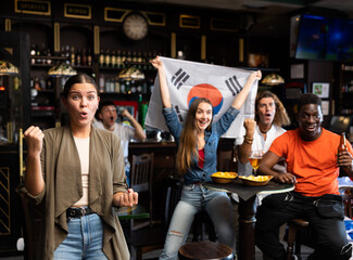 Fototapeta na wymiar Excited young woman, South Korea football team fan spending time in bar with friends. People with state flag in pub.