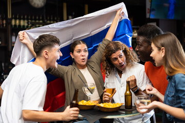 Group of excited young adults watching football championship in sports bar, supporting favorite...