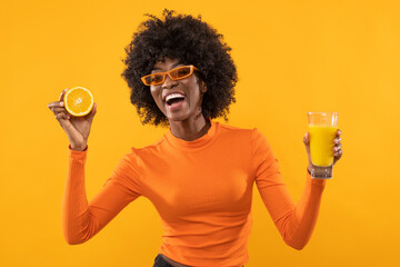 Happy woman is holding fresh orange juice on isolated orange background.