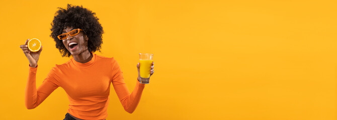 Happy woman is holding fresh orange juice on isolated orange background.