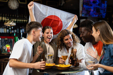 Diverse men and women supporting Japan sports team in pub together. Happy group of friends raising Japan flag.