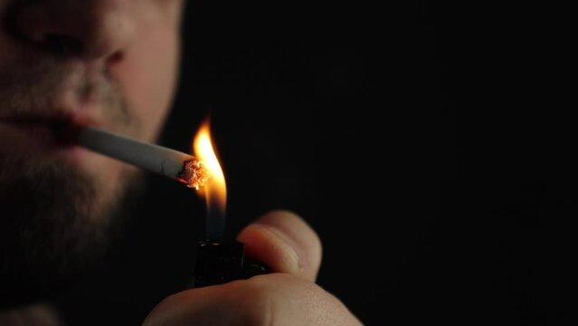 A man smokes a cigarette. Craving for smoking. A cigarette on a black background, smoke is visible. A lot of noxious smoke. Experienced smoker. This is bad for your health. Problems and depression