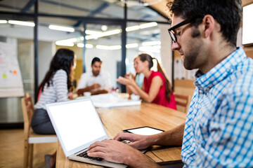 Man working on laptop with colleagues in background