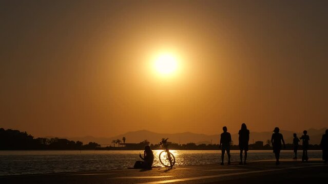 People silhouettes on beach late nightfall. A pretty view of citizen silhouette strolling along the street by the sea water during sunset.