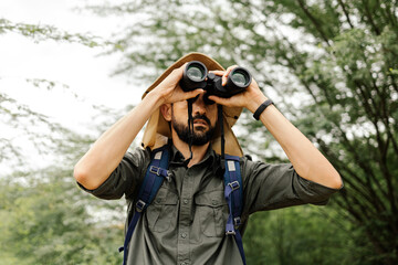 Hiker with backpack using binoculars in the wild. Field biologist or naturalist using binoculars to study wildlife or nature. - obrazy, fototapety, plakaty