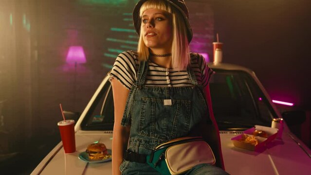 Woman relaxing on car hood with fast food.