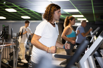 Concentrated motivated adult man leading healthy active lifestyle doing cardio workout in gym, running on treadmill