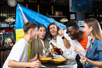 Happy friends of different ages drinking beer and celebrating the victory of the Ukrainian team in the night bar