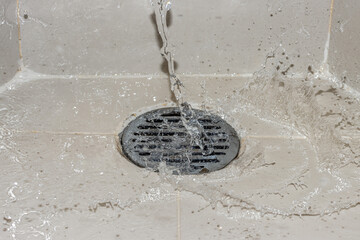 A water of stream is pouring on the shower drain grate