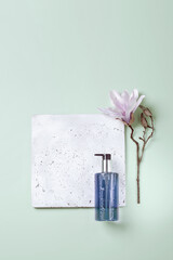 Handwash lotion on grey concrete podium and pale green background with magnolia flower, top view flat lay. Minimalistic, copy space