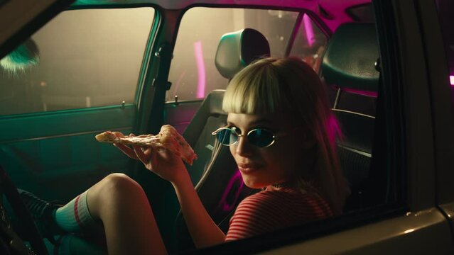 Fashionable woman eating pizza in car.