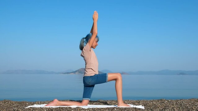 Do anjaneyasana pose on beach. A sporty active young girl enjoy her boddy abd doing anjaneyasana pose on beach in summer.