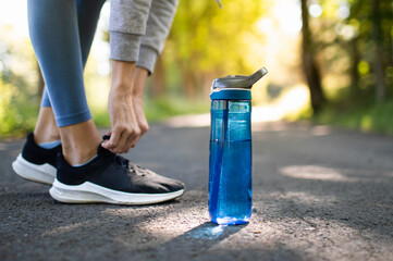 Drinking water and staying hydrated. Person running in the park trying shoe next to bottle of...