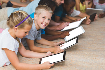 Teacher and kids lying on floor while using digital tablet in library