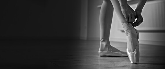 Ballerina tying pointe shoes in dance studio, closeup. Black and white effect. Banner design with...