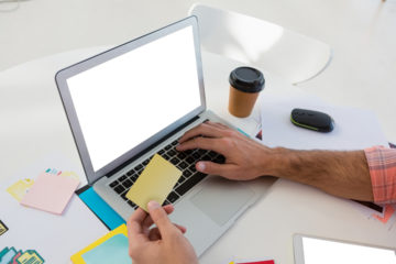Cropped hands of male graphic designer holding sticky note while using laptop