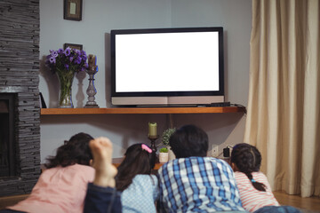 Rear view of family watching television while lying in living room