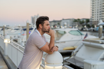 Rich businessman dreaming and thinking near the yacht. Portrait of confident man in modern big american city. Stylish lambersexual model. Sexy man dressed in polo.