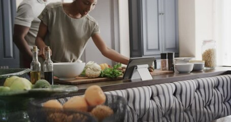 Happy african american couple cooking and using tablet in ktichen in slow motion