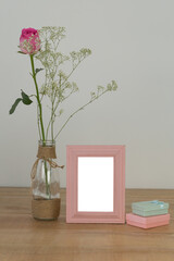 Fototapeta premium Rose flower in glass vase, photo frame and gift boxes on a table