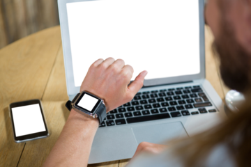 Man using smart watch with laptop and mobile phone on table