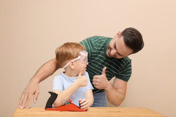Fototapeta premium Father with son showing thumbs up and plane at table near beige wall. Repair work