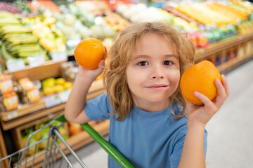 Fototapeta premium Portrait of child with shopping basket purchasing food in grocery store. Funny kids face. Sales and shopping. Kid buying products at supermarket. Supermarket and grocery shop. Discount, sale concept.