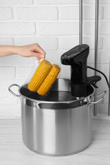 Woman putting vacuum packed corn into pot, closeup. Sous vide cooking