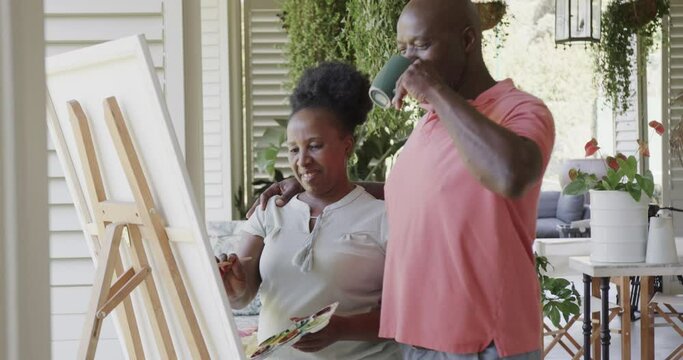 Happy senior african american couple painting and drinking coffee in slow motion