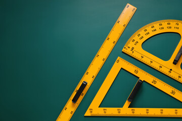Protractor, triangle and ruler on green chalkboard, flat lay. Space for text