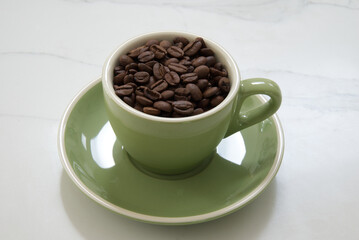 Medium sized green coffee cup filled with whole roasted coffee beans