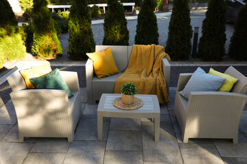 Beautiful rattan garden furniture, soft pillows, blanket and houseplant outdoors