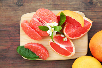 Fresh ripe grapefruits and green leaves on wooden table, flat lay