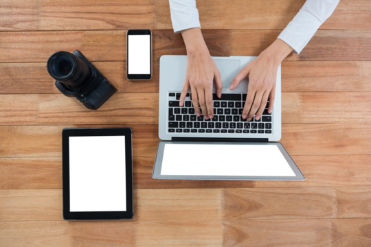 Businesswoman using laptop with camera and touch screen devices on desk