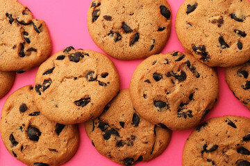 Many delicious chocolate chip cookies on pink background, flat lay