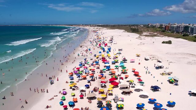 Vista do drone sobre a praia com dunas cheia de turistas e guarda-sol, mar limpo e areia branca na ver&atilde;o na cidade de Cabo Frio, Rio de Janeiro, Brasil