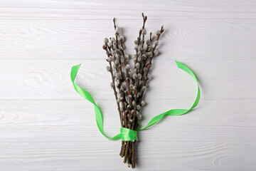 Beautiful blooming willow branches with green ribbon on white wooden table, top view