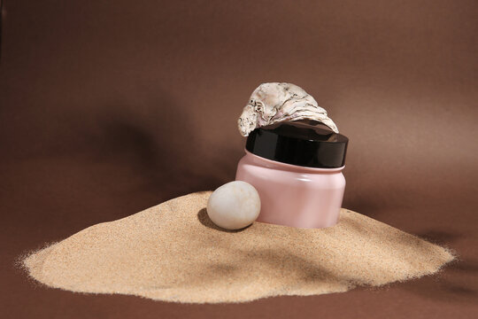 Jar of body cream, seashell and stone on sand against brown background. Space for text