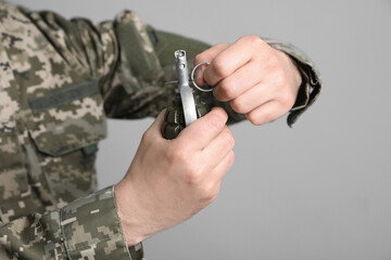 Soldier pulling safety pin out of hand grenade on light grey background, closeup. Military service