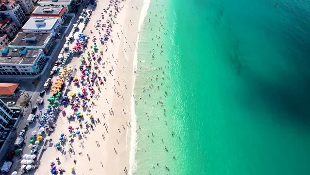 Vista do drone sobre a praia cheia de turistas e guarda-sol, mar limpo e areia branca na cidade de Cabo Frio, Rio de Janeiro, Brasil