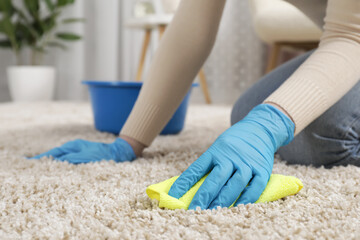 Woman in rubber gloves cleaning carpet with rag indoors, closeup. Space for text