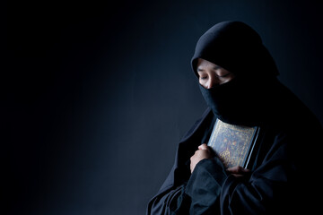 Portrait Asian Muslim woman standing and reading the Quran and appreciates and faith The Holy Al Quran with written Arabic calligraphy meaning of Al Quran, Arabic word translation: The Holy Al Quran.